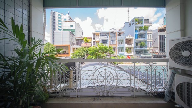 A balcony with a decorative metal railing, a potted plant, and a view of multi-story buildings. - balcony  Studio (Thành phố Hồ Chí Minh)