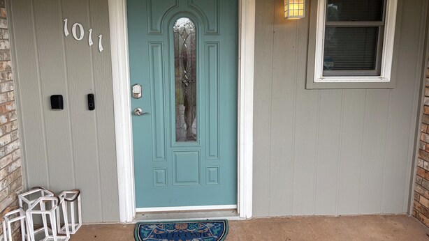 Une porte de couleur bleu sarcelle avec un panneau de verre, un paillasson et une fenêtre avec un luminaire.