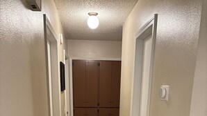 Un couloir étroit doté d’un plancher en bois, de murs blancs et d’un luminaire au plafond.