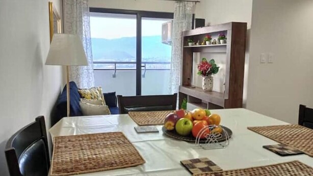 Un comedor con una mesa dispuesta para cuatro, vistas al exterior y una estantería con objetos decorativos.