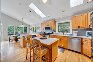 A modern kitchen with wooden cabinets, a central island, and a dining area. - The Lake House on Sunset Point - Lakefront home with private dock & pool table (Moneta)