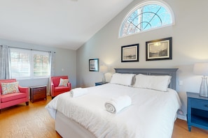 A bedroom with a large bed, two nightstands, a red armchair, and a window with a view.