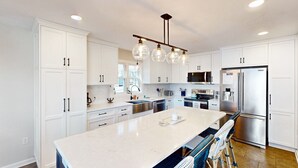 Une cuisine moderne avec des meubles blancs, un grand îlot central, des appareils en acier inoxydable et un luminaire suspendu.
