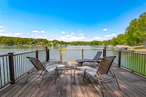 A wooden deck with outdoor furniture overlooking a lake, a caution sign, and a clear sky. - Cottage at the Lake - Waterfront lake-view home with dock, fireplace, pool table, kayaks, & firepit (Moneta)