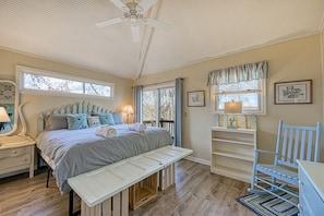 A bedroom with a bed, bench, bedside table, lamp, and a ceiling fan.