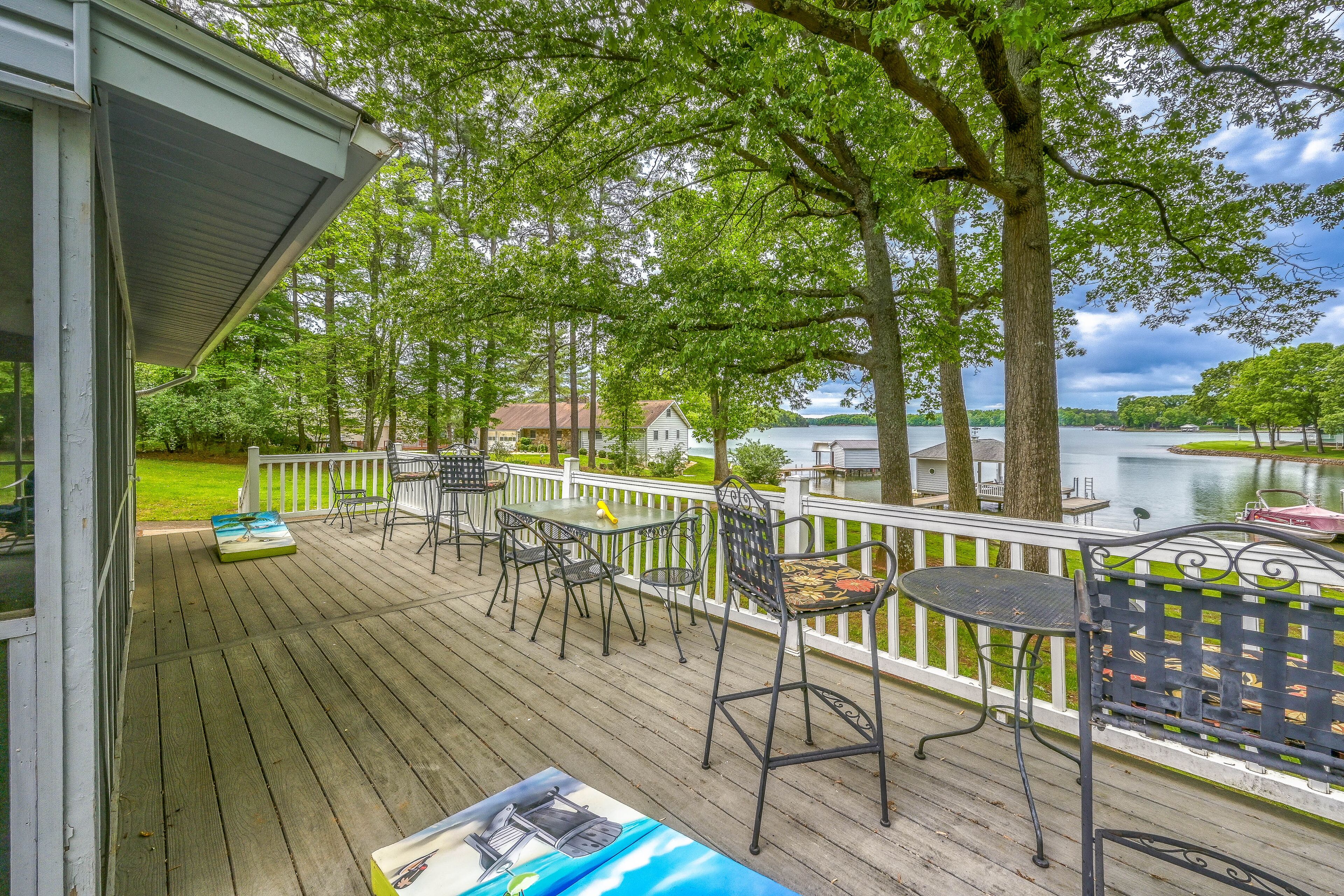 A wooden deck with outdoor furniture, a white railing, and a view of a lake and distant buildings.