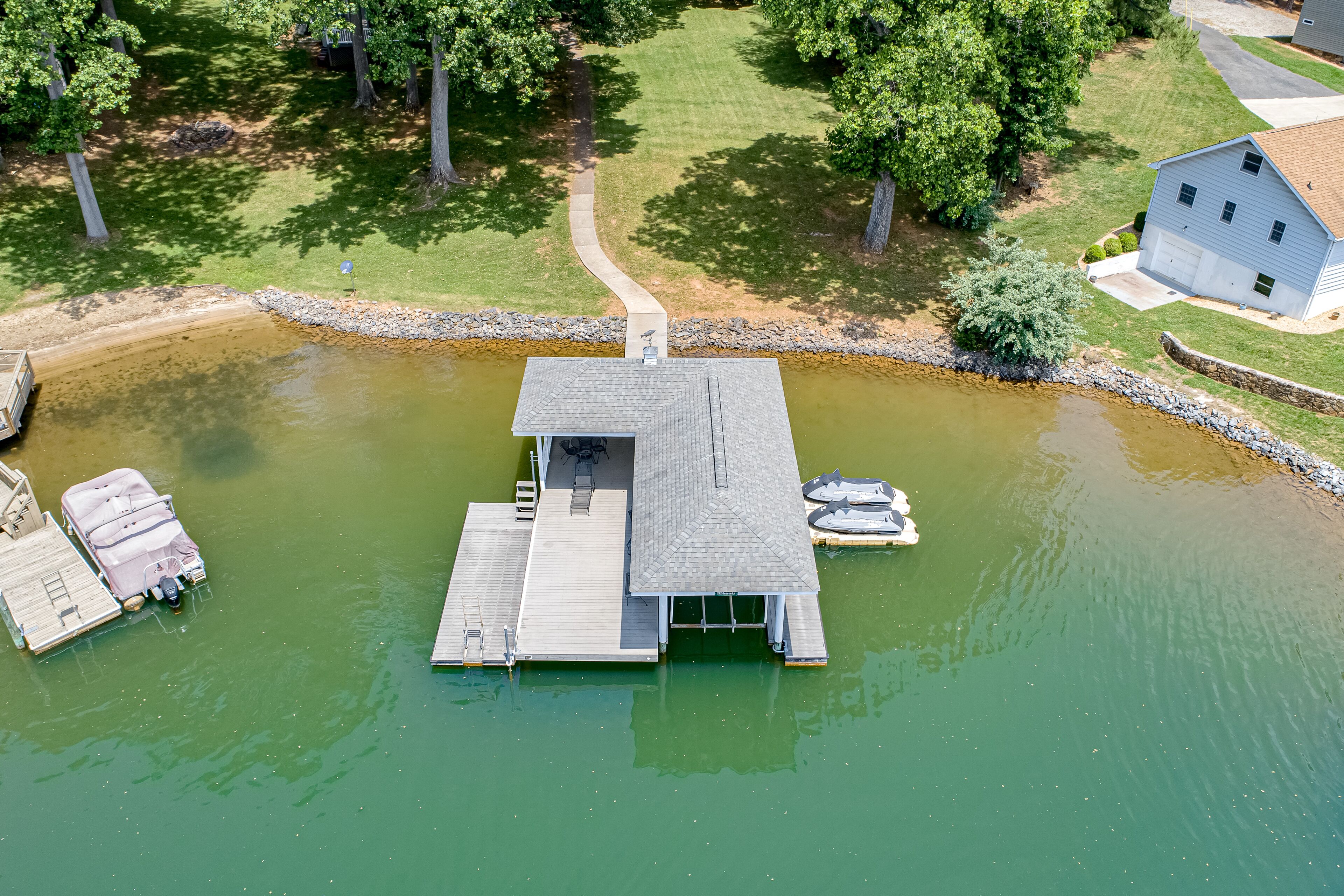 An aerial view of a dock with a small building, boats, and a house in the background.