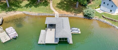 An aerial view of a dock with a small building, boats, and a house in the background.
