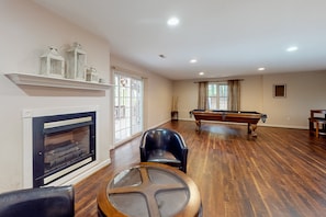 A spacious living room with a fireplace, a pool table, and a billiards table.
