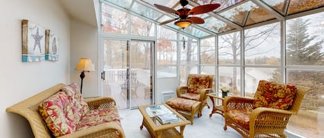 A sunroom with wicker furniture, a ceiling fan, and large windows.