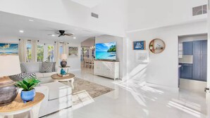 Ein geräumiger Wohnbereich mit Flachbildfernseher, Deckenventilator und Essbereich mit Blick ins Freie.