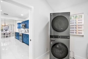 Une cuisine moderne avec des meubles bleus, des appareils en acier inoxydable et un grand appareil combinant lave-linge et sèche-linge.