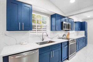 A modern kitchen with blue cabinets, stainless steel appliances, and a white countertop. - NEW! Heron Lagoon Hideaway: Canal Front, Pool, Dog (Sarasota)