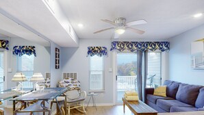 A spacious living area with a glass dining table, a sofa, and a ceiling fan. - Sunset Landing - Waterfront condo with lake-view deck, tennis court & pool (Moneta)