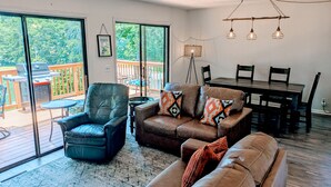 A spacious living room with a large sliding glass door leading to a deck, a dining area with a table and chairs, and a modern chandelier. - Dock Sun Point - Lakefront home for easy boating, fishing, private dock & AC/Wifi, Dogs ok! (Huddleston)