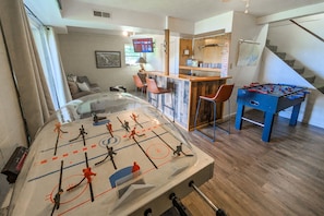 Une pièce comprenant une table de baby-foot, un coin bar et un escalier.