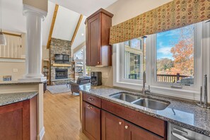 A kitchen with granite countertops, wooden cabinets, a stone fireplace, and a large window with a view of trees. - Osprey Cove - Custom Lakefront home with 2-story dock, Wifi, Game Room and Fireplace (Moneta)