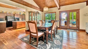 A spacious dining area with a wooden table and chairs, a large wooden cabinet, and a view through glass doors to an outdoor patio. - The Main House - Lakefront home with private hot tub & balcony (Huddleston)
