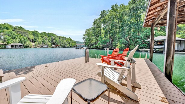 A wooden deck with chairs and a table overlooking a lake, surrounded by trees and docked boats. - The Main House - Lakefront home with private hot tub & balcony (Huddleston)