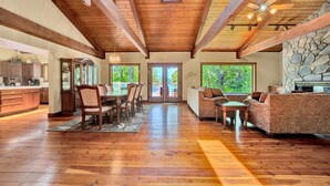 A spacious living area with a wooden floor, a dining table with chairs, a sofa, and a fireplace. - The Main House - Lakefront home with private hot tub & balcony (Huddleston)