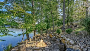 Un hogar rodeado de piedra y madera, situado en un paisaje natural con árboles y un lago.