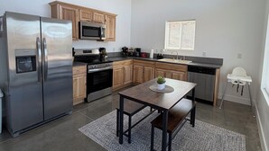Una cocina moderna con electrodomésticos de acero inoxidable, armarios de madera, una mesa de comedor con sillas y una ventana pequeña.