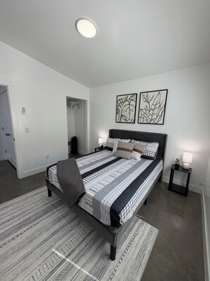 Une chambre à coucher comprenant un lit, des tables de chevet, une commode, un tapis et deux œuvres d’art murales.