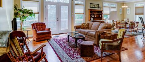 A spacious living room with hardwood floors, a large sofa, a coffee table, and a dining area with chairs and a table.