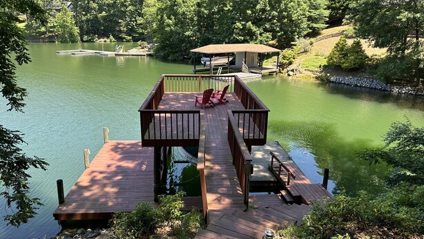 Una terraza de madera con sillas que da a un lago, rodeada de árboles.