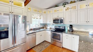 Una cocina moderna con armarios blancos, electrodomésticos de acero inoxidable, encimeras de granito y piso de madera.