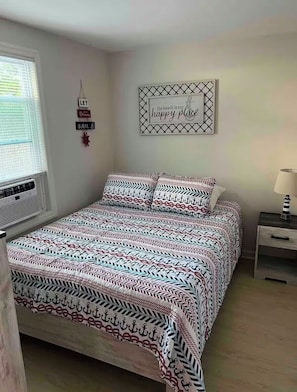 A neatly made bed with patterned bedding, a wall-mounted sign saying 'the beach is my happy place,' and a small bedside table with a lamp.