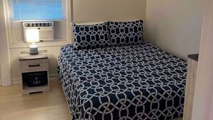 Une chambre à coucher comprenant un lit, une table de chevet, une lampe, une fenêtre avec des stores et un élément de décoration murale.