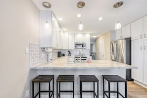 Una cocina moderna con armarios blancos, una isla de granito y taburetes de bar.