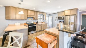 A kitchen with wooden cabinets, a central island, stainless steel appliances, and pendant lighting.