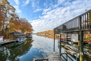 Ein ruhiger Fluss mit Booten, die am linken Ufer vertäut sind, einem hölzernen Steg auf der rechten Seite und herbstlichen Bäumen, die sich im Wasser spiegeln.
