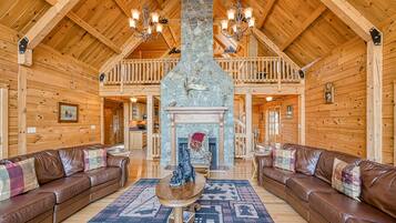 Un intérieur spacieux de chalet en bois, avec une cheminée en pierre, des canapés en cuir et un haut plafond en bois.