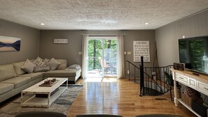 A living room with a sofa, coffee table, and TV stand. There is a sign on the wall and a painting above the sofa. - Humble Hideaway - Inviting lakefront home with firepit, balcony & W/D - dog-friendly (Moneta)