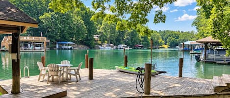 A wooden dock with chairs and a small boat, surrounded by calm water and greenery.