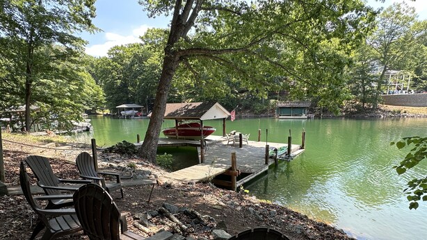 A lakeside setting with docked boats, a covered area, and Adirondack chairs. - Humble Hideaway - Inviting lakefront home with firepit, balcony & W/D - dog-friendly (Moneta)