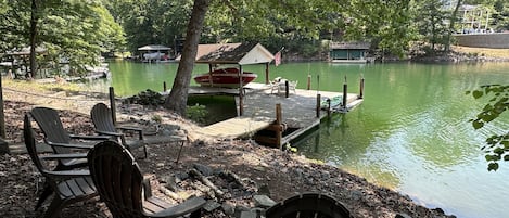 A lakeside setting with docked boats, a covered area, and Adirondack chairs.