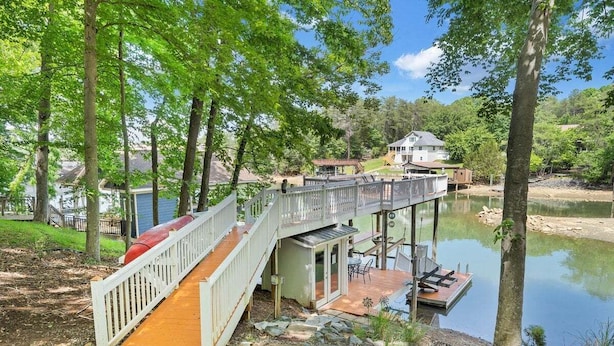 Une terrasse en bois avec une porte vitrée donnant sur un espace extérieur abrité, une jetée s’avançant dans un lac et une maison en arrière-plan.