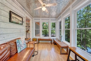 A room with a wooden ceiling, large windows, a brown leather sofa, and a bench.