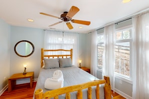 A bedroom with a wooden bed frame, a round mirror, a ceiling fan, and a view of the outdoors through large windows. - Bears Den at Acorn Dr - Lakefront, Pet Friendly Cottage with Hot Tub, Balcony, and Dock (Moneta)