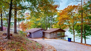 A cabin by a lake with a gravel driveway and a wooden dock. - Bears Den at Acorn Dr - Spacious pet friendly Cottage with balcony, dock, and hot tub (Moneta)