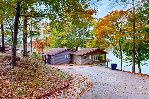 A cabin by a lake with a gravel driveway and a wooden dock. - Bears Den at Acorn Dr - Lakefront, Pet Friendly Cottage with Hot Tub, Balcony, and Dock (Moneta)