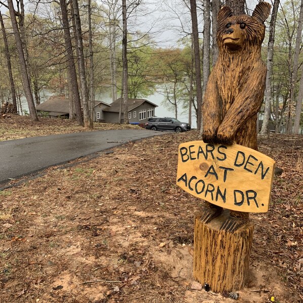 A wooden bear sculpture holding a sign that reads "BEARS DEN AT ACORN DR." - Bears Den at Acorn Dr - Lakefront, Pet Friendly Cottage with Hot Tub, Balcony, and Dock (Moneta)
