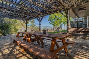 Et overdækket udendørs område med picnicborde, en pergola og en bygning med balkon.