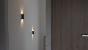 A hallway with a wooden door, a wall-mounted light fixture, and a ceiling light. - Mr. W | Moderno departamento de 2 pisos y terraza (Guadalajara)