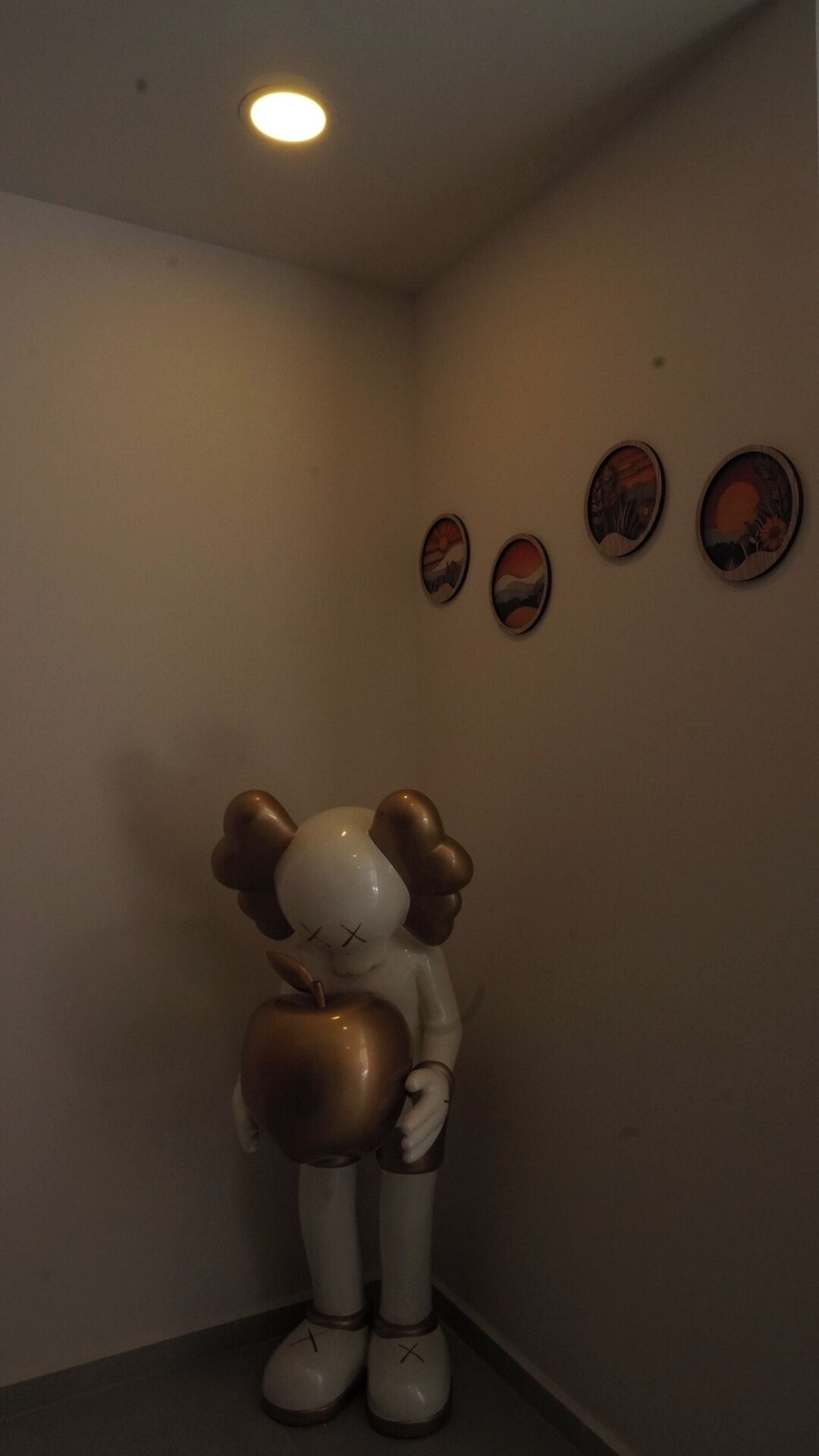 A corner with a wall-mounted clock, a small statue, and three framed pictures.