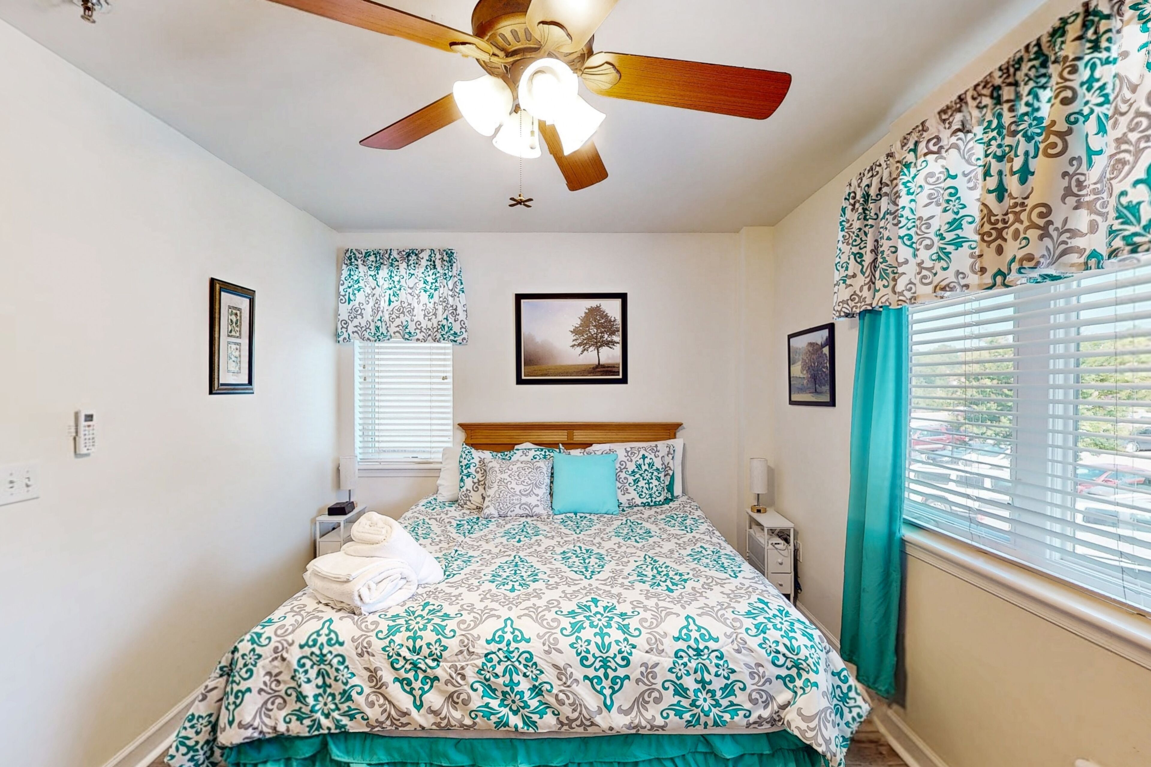 A bedroom with a bed, ceiling fan, window with blinds, and curtains.